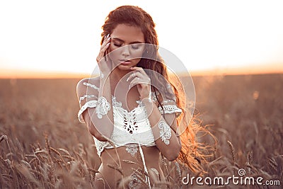 Boho chic style. Portrait of bohemian girl with white art posing over wheat field enjoying at sunset. Outdoors photo. Tranquility Stock Photo