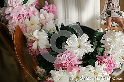 Boho girl holding pink and white peonies in hands at rustic wooden chair. Stylish hipster woman in bohemian dress arranging peony Stock Photo