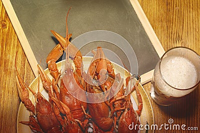 Boiled crawfish, glass of light beer and black chalkboard on a wooden table. Stock Photo