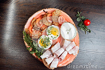 Boiled eggs with green onions, fried potato pancakes, bread with delicious bacon. Dish is decorated with fresh herbs Stock Photo