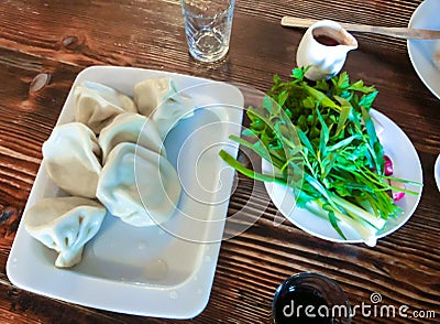 Boiled khinkali on a tray. Georgian traditional cuisine, domestic khinkali. Greens on the plates. Stock Photo