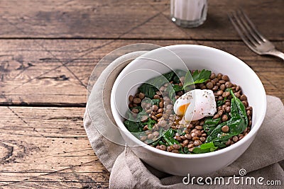 Boiled lentils with spinach, herbs, spices and poached egg in ceramic bowls on a wooden background Stock Photo