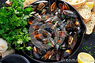 Boiled mussels in iron pan cooking dish. with herbs, butter, lime, parsley, garlic and fresh bread. Stock Photo