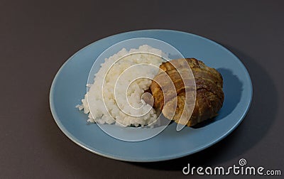 Boiled white rice with chicken cutlet wrapped in bacon on a gray background blue plate Stock Photo