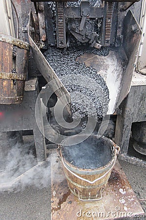 Boiling hot asphalt is filled into a bucket from an asphalt machine to fill a pothole. Road construction, road rehabilitation, as Stock Photo