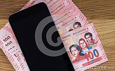 Bolivian currency, One hundred Bolivianos banknotes lying together with a mobile phone on the wooden table Stock Photo