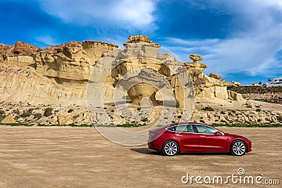Bolnuevo, Murcia, Spain - February 7, 2020: panoramic view of a red Tesla Model 3 electric car with rock formation on the Editorial Stock Photo