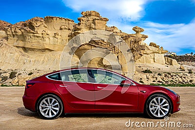 Bolnuevo, Murcia, Spain - February 7, 2020: side view of a red Tesla Model 3 electric car with rock formation on the mediterranean Editorial Stock Photo