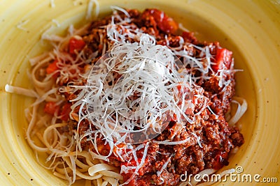 Bolognese pasta sprinkled with grated parmesan in yellow deep plate, selective focus Stock Photo