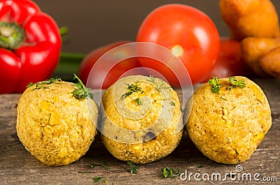 Bolon, an ecuadorian typical food with a blurred tomato and pepper behind, over a wooden table Stock Photo