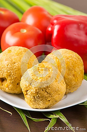 Bolon, an ecuadorian typical food on a white plate with a blurred tomato and pepper behind, over a green leaf Stock Photo