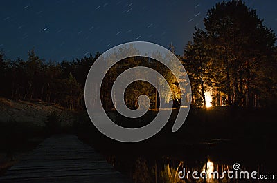 Bonfire in the night forest. Wooden bridge over the river that leads into the Woods Stock Photo