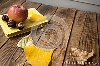 A book apple yellow leaves chestnut on wooden background Stock Photo