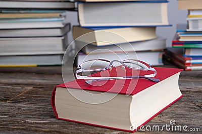 Book and reading glasses in front of piles of different books Stock Photo