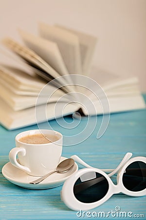 Book, sunglasses and cup of coffee on a wooden blue background. Stock Photo