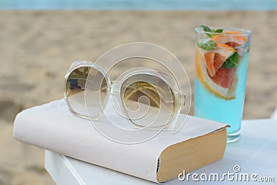 Book, sunglasses and glass of refreshing drink on beach Stock Photo