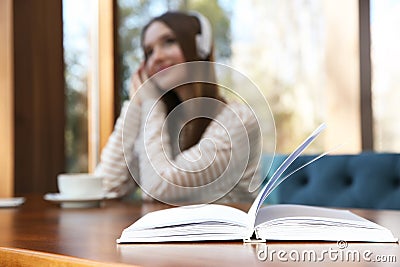 Book on table in cafe and woman with headphones on background Stock Photo