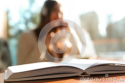 Book on table and woman with headphones on background. Audiobook concept Stock Photo