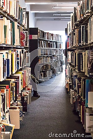 Books on library shelves with leg of person visible further down the isle. Modern building Editorial Stock Photo