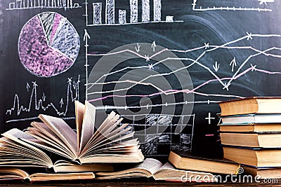 Books on the table against the background of a chalkboard on which are drawn graphs and charts of growth and decline. Business Stock Photo