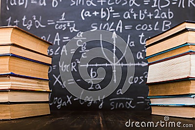 Books on a wooden table, against the background of a chalk board with formulas. Teacher's day concept and back to school Stock Photo