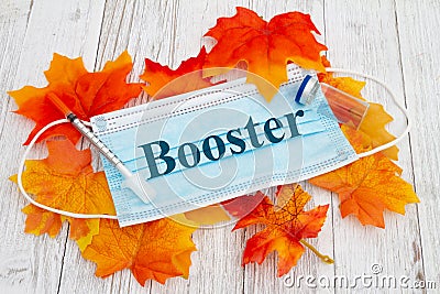 Booster message on medical face mask with needle and vaccine bottle with fall leaves Stock Photo