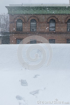 Boot-prints leading toward the edge of a rooftop during heavy snowfall Stock Photo