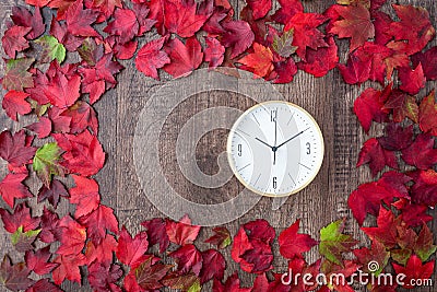 Border of fall color in red, green, yellow, and orange maple leaves on a rustic wood background, with round white analog clock Stock Photo
