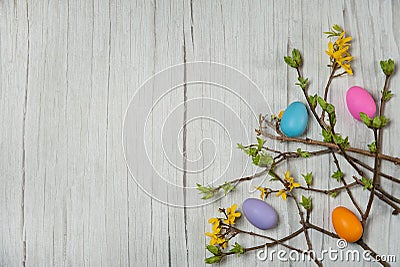 The border is made of forsythia branches with yellow flowers and multicolored Easter eggs on a light wooden background. Stock Photo