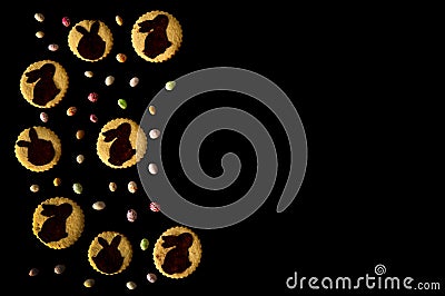 The border is made of homemade cookies and a scattering of colored chocolate eggs on a black background. Stock Photo