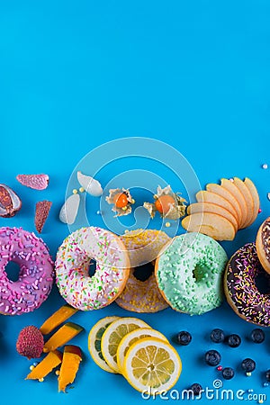 Bordure of colorful fresh donuts with different kinds of topping and fruits on blue paper background. Stock Photo