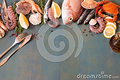 Bordure of fresh seafood, crab, fish and olives oil with fish knife and fork on a blue wooden background with copy space. Stock Photo
