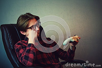 Bored adolescent boy seated in his armchair late night playing video games inside a dark room background. Sleepy boy holding Stock Photo