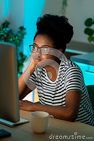 Bored African American lady freelancer sits at home office thinking about project looking at desktop Stock Photo