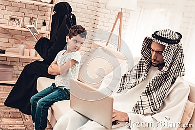 Bored Arabian Boy Sitting with Family on Sofa. Stock Photo