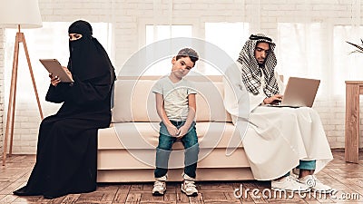 Bored Arabian Boy Sitting with Family on Sofa. Stock Photo