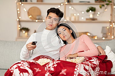 Bored Asian Couple Watching TV Celebrating Christmas At Home Stock Photo