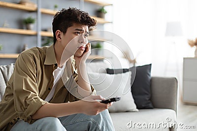 Bored asian man watching television sitting on couch Stock Photo
