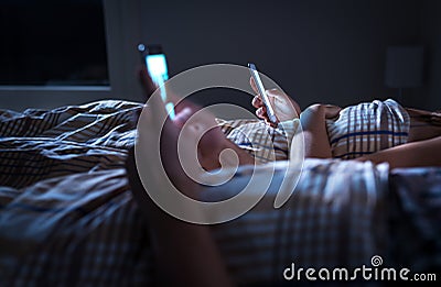 Bored distant couple ignoring each other lying in bed at night while using mobile phones. Smartphone addict. Stock Photo