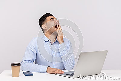 Bored exhausted man employee sitting office workplace with laptop on desk, yawning covering face with hand Stock Photo