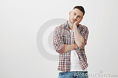 Bored and exhausted young handsome male with bristle in stylish glasses leaning head on palm while being tired and Stock Photo