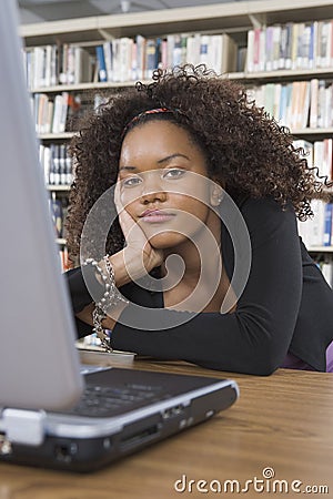 Bored Female Student Sitting At Library Desk Stock Photo