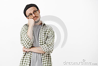 Bored frustrated gloomy handsome bearded guy in glasses black beanie and checked green shirt leaning head on fist gazing Stock Photo