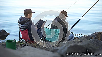 Bored men catching fish, using tablet to search tutorials on fishing websites Stock Photo