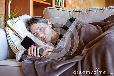 Bored pretty girl looking at the mobile stretched out on the sofa at home Stock Photo