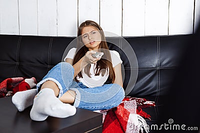 Bored pretty girl watching tv, sitting on sofa at home. Stock Photo