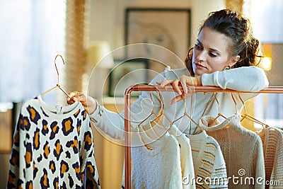 Bored stylish female choosing sweaters hanging on clothes rack Stock Photo