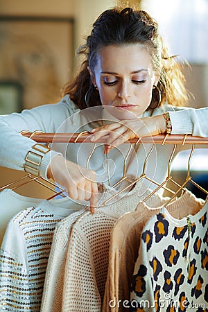 Bored stylish woman choosing sweaters hanging on rack Stock Photo