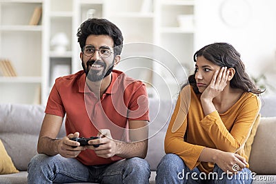 Bored young indian woman looking at boyfriend playing video games at home Stock Photo