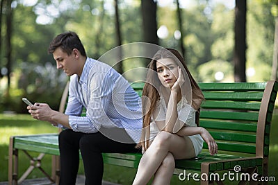 Bored young woman on dull date, suffering from her boyfriend`s neglect or smartphone addiction at park Stock Photo